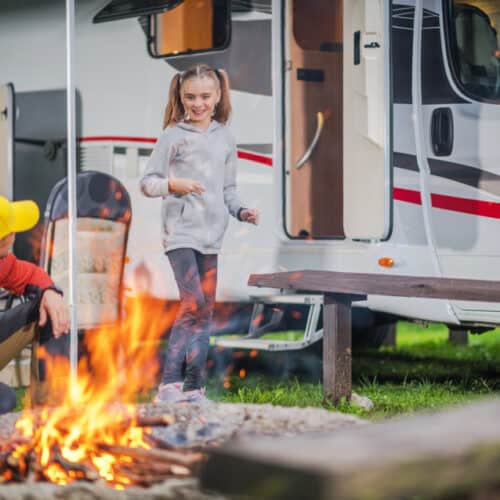 Father and son building a camp fire with an RV in the background