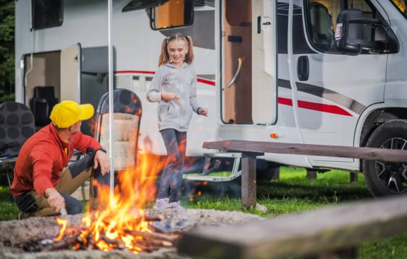 Father and son building a camp fire with an RV in the background