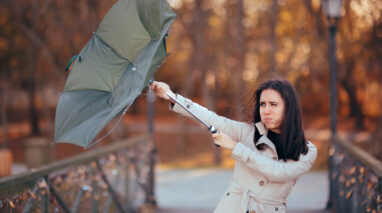 Business woman fights the wind while her umbrella turns inside out