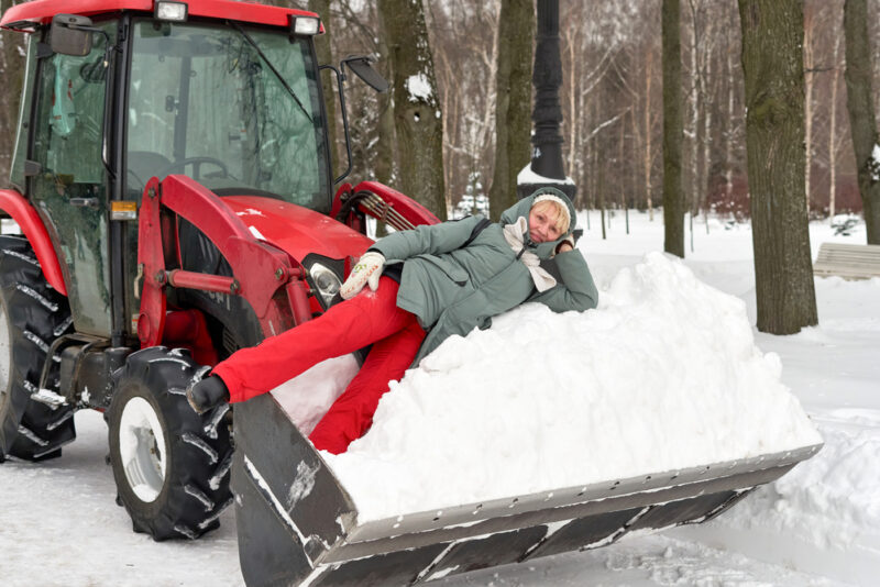 Woman lays in snow in the shovel of a snow plow.