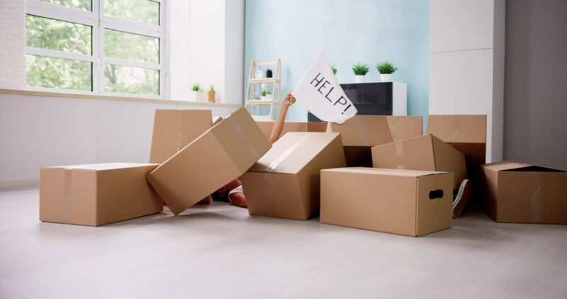 Pile of moving boxes on floor of new home with hand raised up through them holding a help sign - cheap homeowners insurance in Washington.