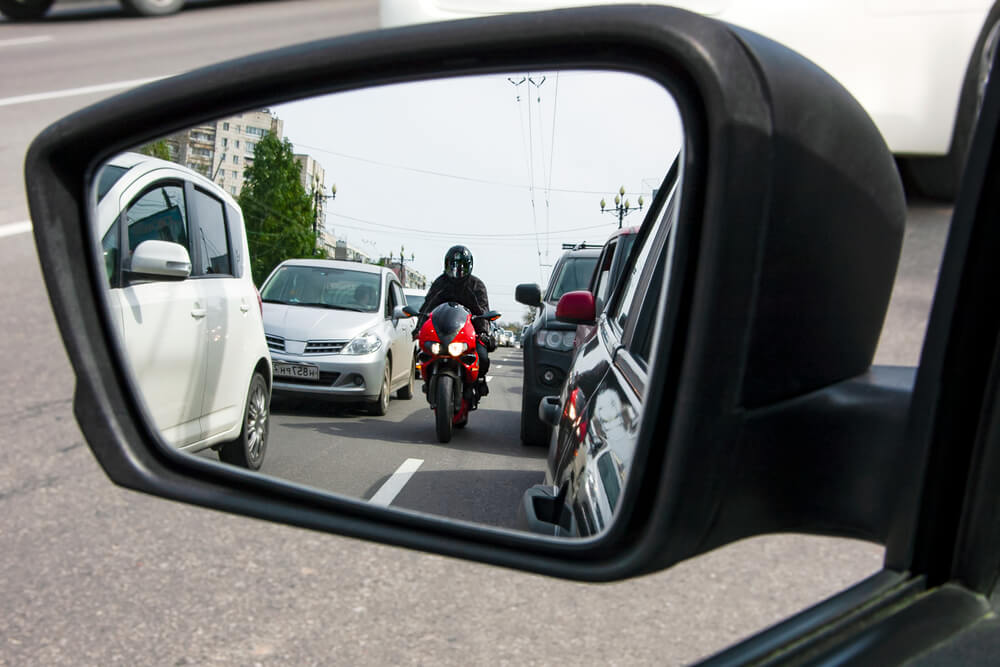 A red, sporty, motorcycle moves between the lane, dangerously close to cars. Lane splitting