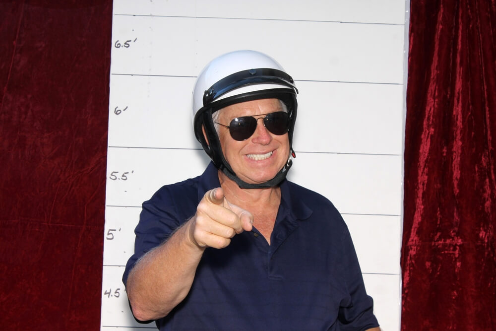 Smiling motorcycle cop in photo booth points finger at person giving excuses for no insurance.