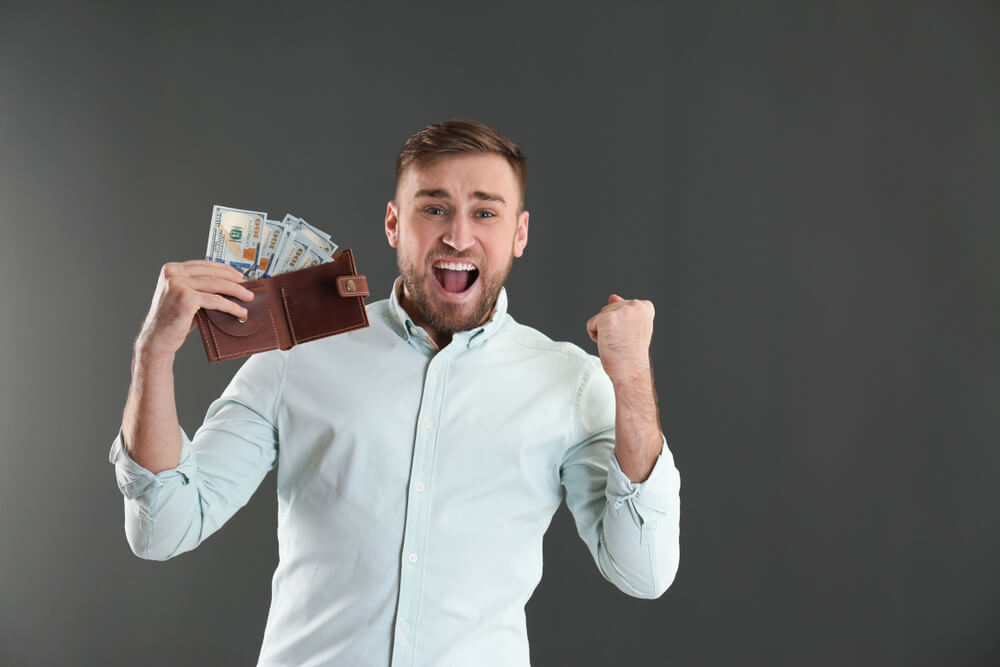 Young man very happy to save money with bundling. Holding his wallet with money bulging out.