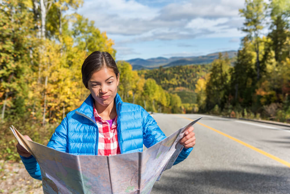 Asian woman on the side of the road looking at map with a scrunched up nose.