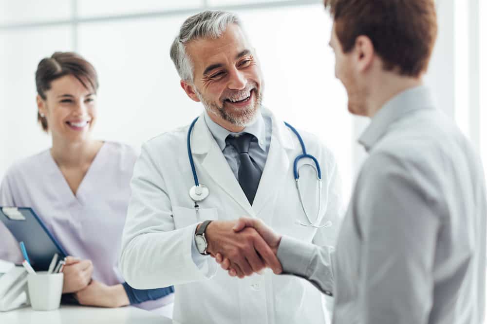 Smiling doctor shaking a patient's hand with a nurse in the background